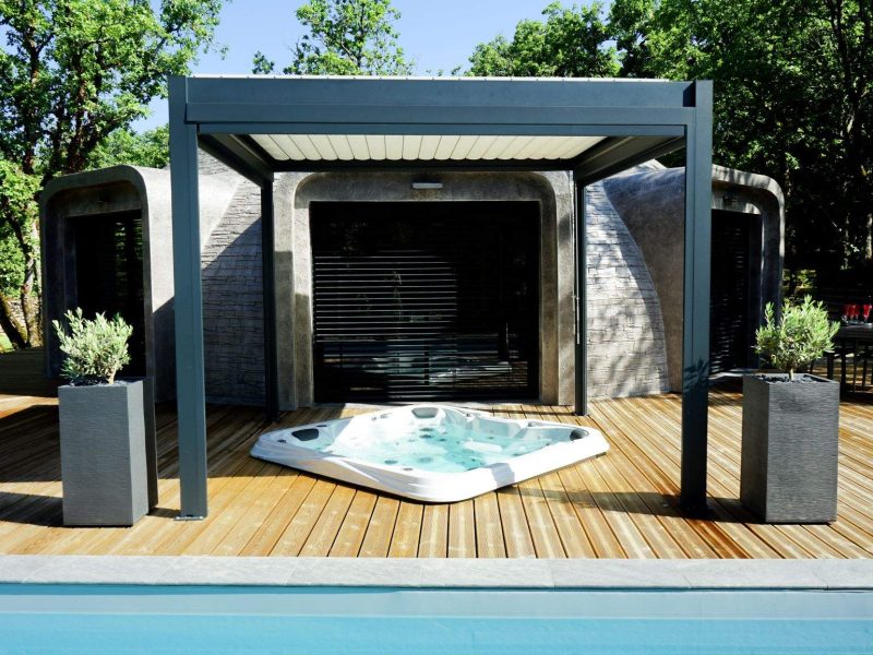Hébergement insolite avec jacuzzi sur une terrasse en bois, entouré de verdure.