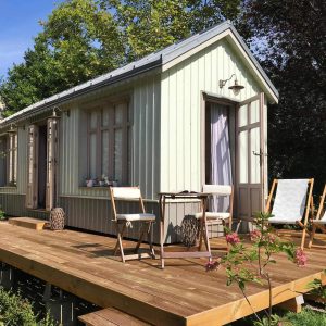 Charmante cabane en bois avec terrasse ensoleillée, entourée de verdure.