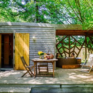 Cabane en bois dans les arbres, avec terrasse en bois et mobilier extérieur.
