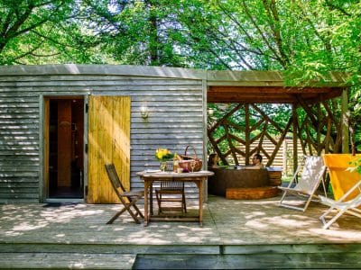 Cabane en bois dans les arbres, avec terrasse en bois et mobilier extérieur.