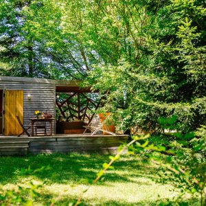 Cabane en bois dans la verdure, avec une terrasse ensoleillée et des chaises confortables.