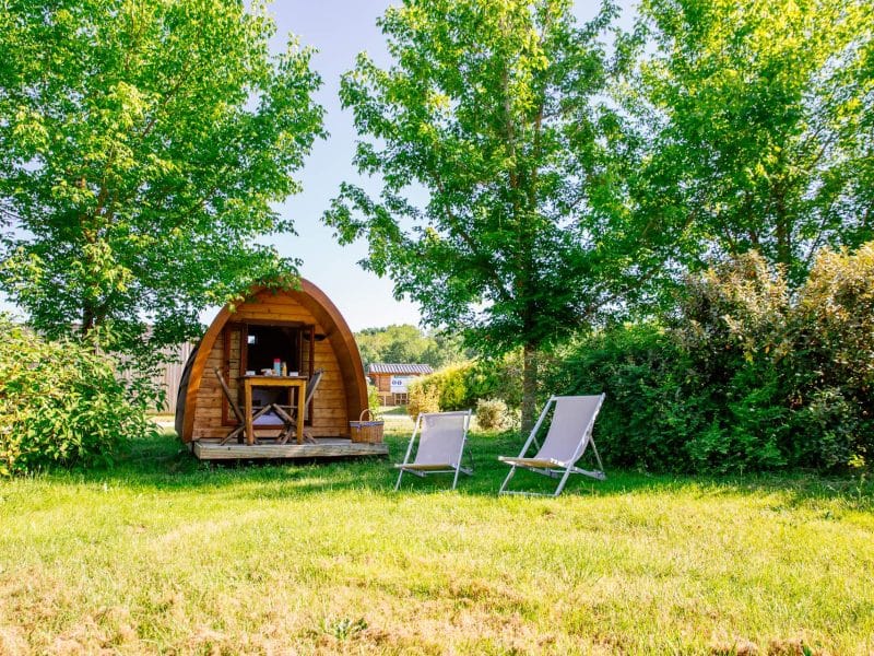 Cabane en bois en Aquitaine, entourée darbres et de chaises longues.