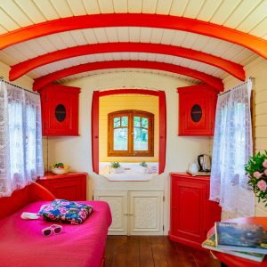 Hébergement insolite en roulotte, intérieur cosy avec murs rouges et fenêtres lumineuses.