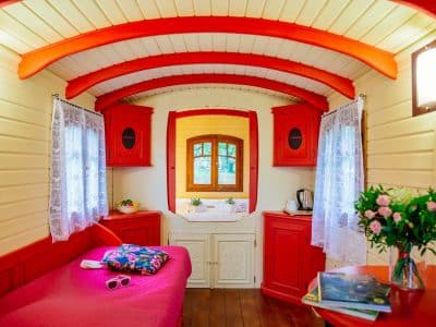 Hébergement insolite en roulotte, intérieur cosy avec murs rouges et fenêtres lumineuses.