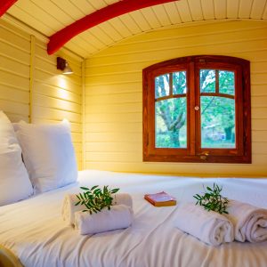 Hébergement insolite en Aquitaine : une charmante roulotte avec lit douillet et fenêtres en bois.