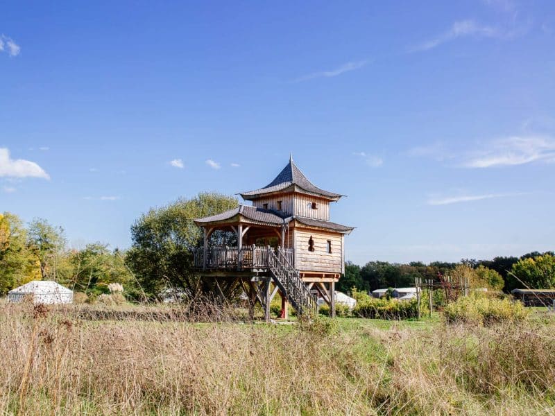Cabane perchée en bois avec un toit pointu, entourée de verdure en Aquitaine.