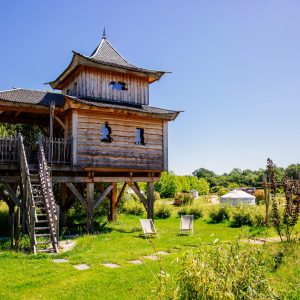 Cabane perchée en bois avec terrasse, entourée de verdure en Aquitaine.