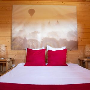 Chalet en bois avec lit douillet et coussins rouges, décoré dune grande toile.