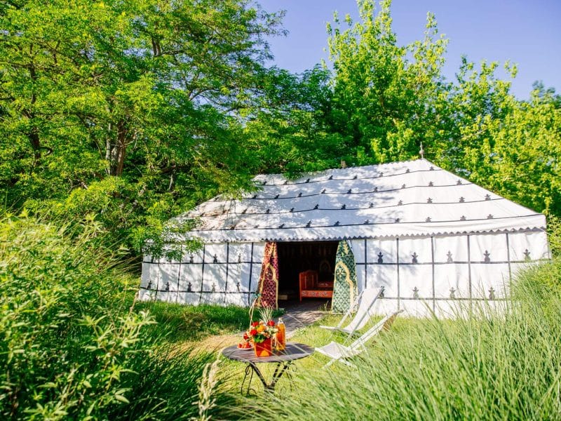 Yourte spacieuse en Aquitaine, entourée de verdure, avec chaises et table décorative.