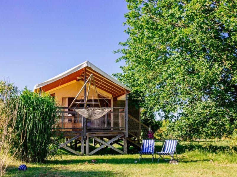 Cabane sur pilotis en Aquitaine, avec hamac suspendu et chaises rayées.