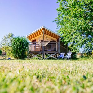 Cabane en bois avec terrasse, entourée de verdure et d’un hamac.