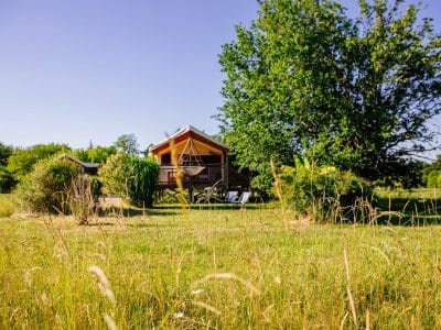 Cabane en bois au milieu dun jardin verdoyant, avec un hamac suspendu.