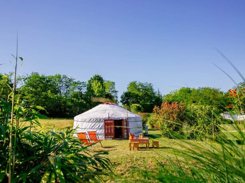 Yourte spacieuse en Aquitaine, entourée de verdure et de mobilier en bois.