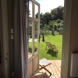 Hébergement insolite en Basse-Normandie, vue sur jardin verdoyant depuis la porte ouverte.