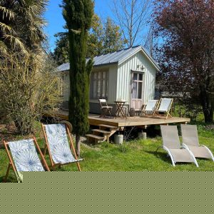 Cabane en bois à Basse-Normandie, entourée de verdure et chaises longues confortables.