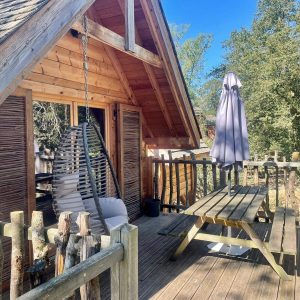 Cabane perchée en Auvergne-Rhône-Alpes avec terrasse en bois et fauteuil suspendu.