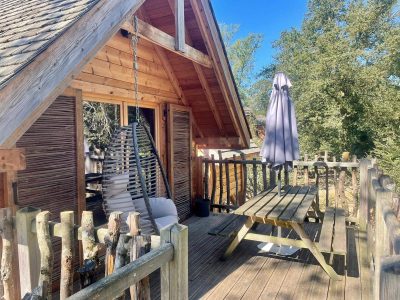 Cabane perchée en Auvergne-Rhône-Alpes avec terrasse en bois et fauteuil suspendu.