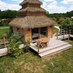 Cabane en bois avec toit de chaume, terrasse en bois et vue sur la nature.