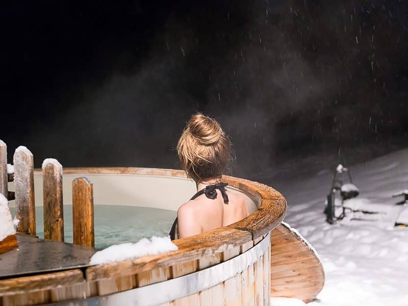Bain nordique en bois sous la neige, offrant une vue apaisante sur la nuit étoilée.
