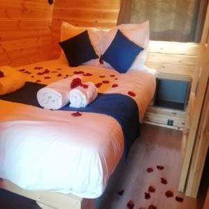 Chalet en bois romantique avec pétales de rose sur le lit et ambiance chaleureuse.
