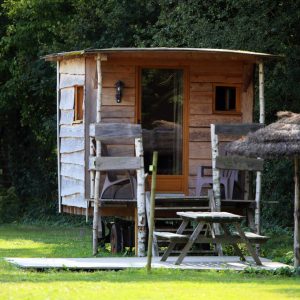 Cabane en bois dans un cadre verdoyant, avec terrasse et parasol.