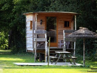 Cabane en bois dans un cadre verdoyant, avec terrasse et parasol.