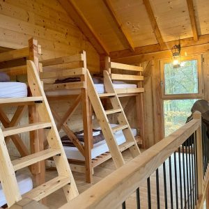 Cabane en bois avec lits superposés, lumière chaleureuse et vue sur la nature.