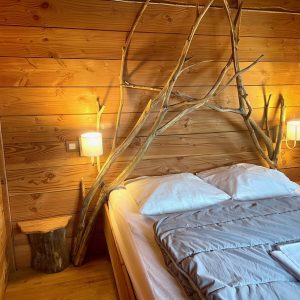 Chalet en bois avec un lit douillet et une tête de lit en branches naturelles.