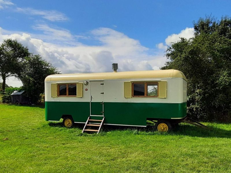 Caravane vintage verte et blanche, entourée dun vaste espace verdoyant.