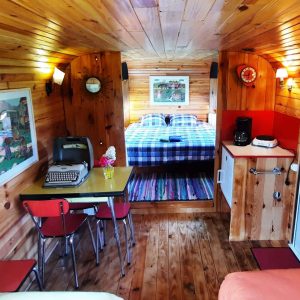 Hébergement insolite en bois avec lit double et décoration colorée. Ambiance chaleureuse.