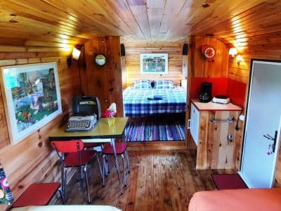 Hébergement insolite en bois avec lit double et décoration colorée. Ambiance chaleureuse.