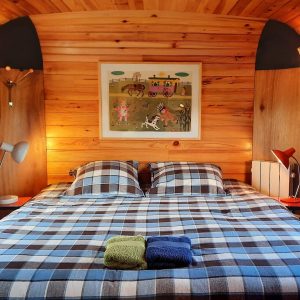 Chalet en bois chaleureux avec lit à carreaux et décor coloré. Parfait pour un séjour insolite.