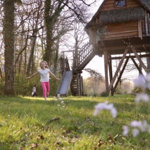 Cabane dans les arbres en Auvergne, entourée de fleurs et denfants jouant.