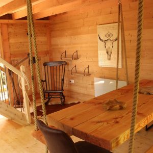 Cabane en bois avec une grande table et des chaises suspendues, ambiance chaleureuse.