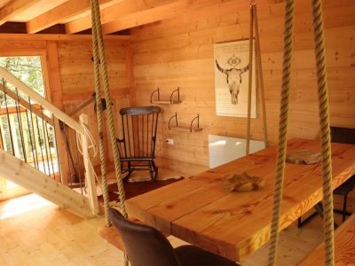 Cabane en bois avec une grande table et des chaises suspendues, ambiance chaleureuse.
