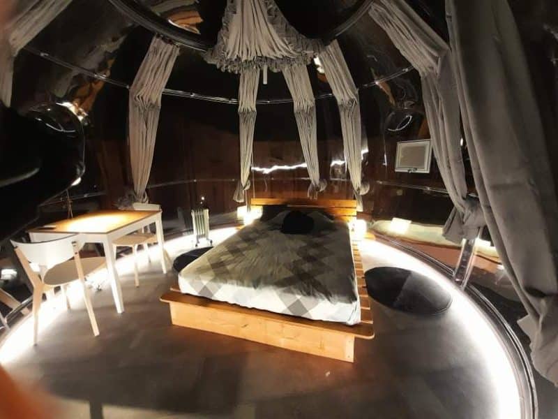 Hébergement insolite en bulle, intérieur moderne avec lit en bois et éclairage doux.