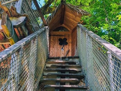 Cabane perchée en bois avec un toit en chaume et un escalier en bois.