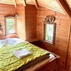 Cabane en bois chaleureuse avec un lit douillet et des fenêtres lumineuses.