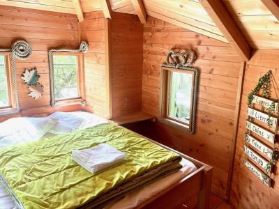 Cabane en bois chaleureuse avec un lit douillet et des fenêtres lumineuses.