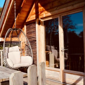 Cabane en bois avec un fauteuil suspendu sur la terrasse ensoleillée.