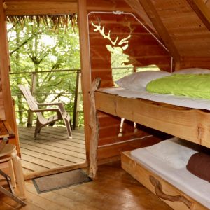 Cabane en bois avec lit douillet et balcon surplombant la nature verdoyante.