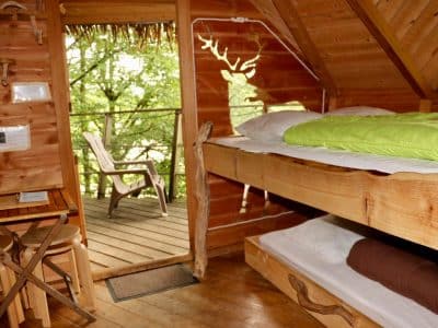Cabane en bois avec lit douillet et balcon surplombant la nature verdoyante.