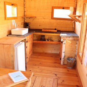 Cabane en bois chaleureuse avec cuisine équipée et lumière naturelle.