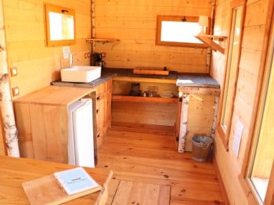 Cabane en bois chaleureuse avec cuisine équipée et lumière naturelle.
