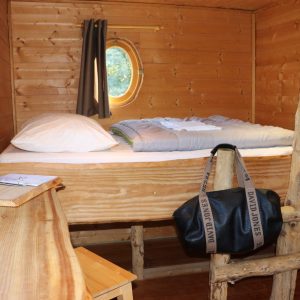 Cabane en bois avec lit douillet et vue sur la nature, ambiance chaleureuse.