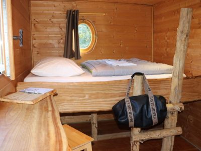 Cabane en bois avec lit douillet et vue sur la nature, ambiance chaleureuse.
