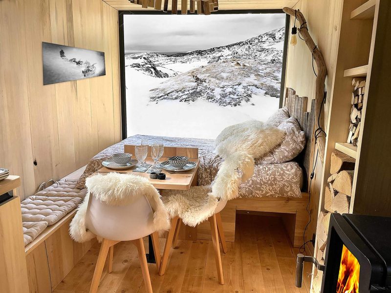 Cabane en bois avec vue sur des montagnes enneigées et décor cosy.