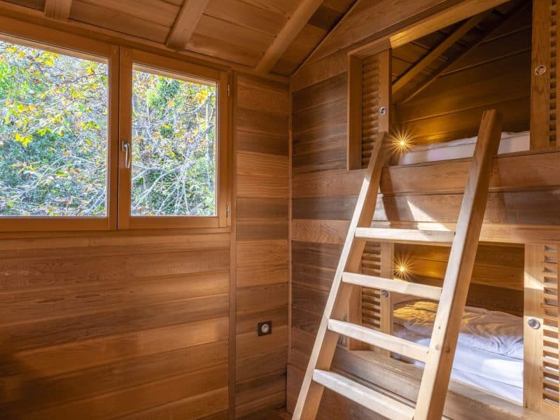Cabane en bois avec échelle menant à des lits superposés et vue sur la nature.