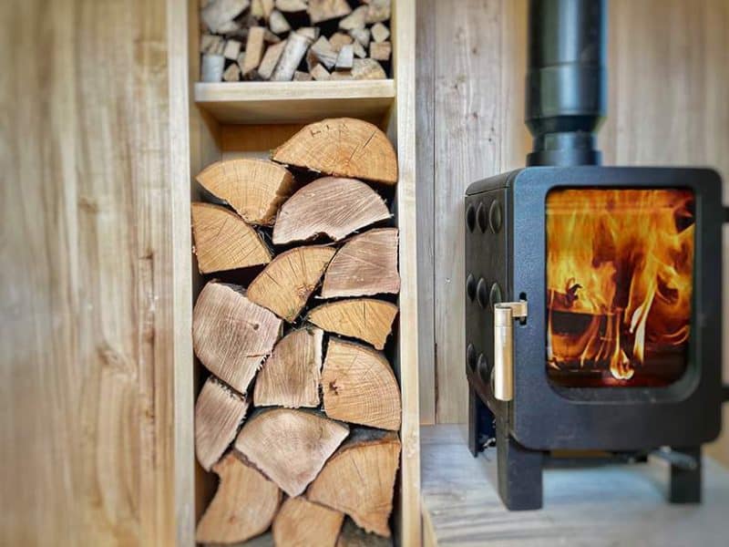 Chalet chaleureux avec un poêle à bois et du bois empilé à côté.