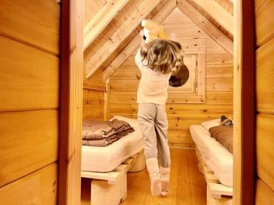 Cabane en bois dans les Alpes, enfant sautant joyeusement entre les lits.
